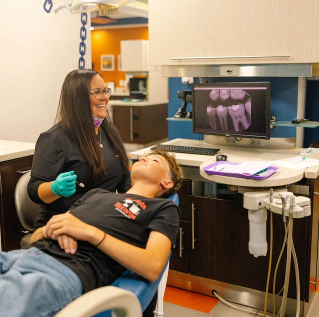 A pediatric orthodontist smiling at a patient in a dental chair next to an educational graphic explaining interceptive orthodontics at Smile Zone, Springfield, MO.